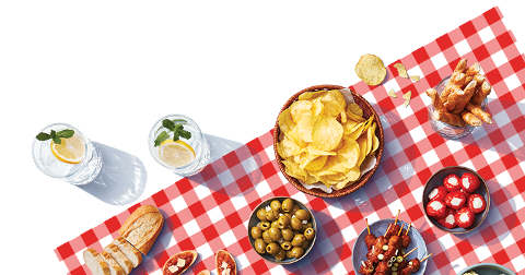 Picknick tafel met aardappelchips, groene olijven, gevulde pepers, stokbrood en drankjes met citroen en munt.