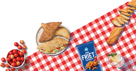 Picknicktafel met diverse snacks zoals broodjes, AH Mini Friet Paprika, kerstomaatjes en een glas water met citroen en munt.