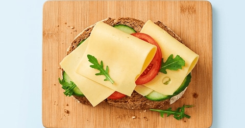 Volkorenboterham met plakjes kaas, komkommer, tomaat en rucola op een houten snijplank