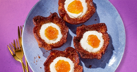 Vier gebakjes op een blauw bord, gevuld met witte vulling en een gele jam in het midden, op een paarse achtergrond.