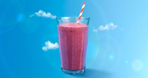 Glas met roze smoothie en rood-wit gestreept rietje tegen een blauwe achtergrond met wolkjes.