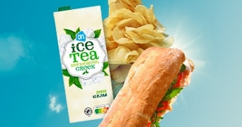 AH Ice Tea Refreshing Green, stapel chips en een broodje met sla en groente tegen een blauwe hemel.