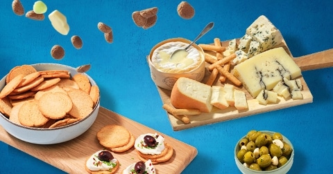 Borrelplank met verschillende kazen, crackers, olijven en belegde toastjes op een blauwe achtergrond