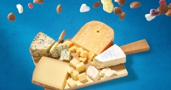 Borrelplank met verschillende soorten kaas op een houten plank, met strooigoed zoals kruidnoten en suikerhartjes op een blauwe achtergrond