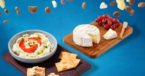 Plank met brie, rode druiven, crackers en een kom romige dip met kruiden op een blauwe achtergrond