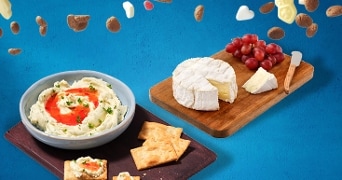 Plank met brie, rode druiven, crackers en een kom romige dip met kruiden op een blauwe achtergrond