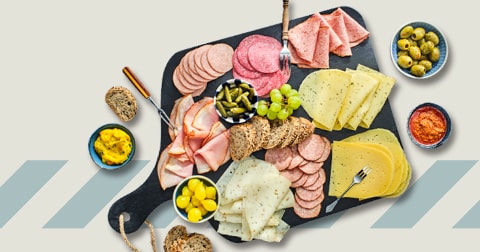 Borrelschotel met diverse vleeswaren, kazen, brood, druiven, augurken en olijven op een serveerplank, met dips aan de zijkant.