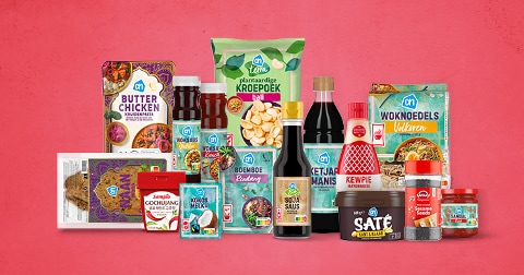 Verschillende Aziatische producten van Albert Heijn en A-merken, waaronder woknoedels, plantaardige kroepoek, kokosmelk, sojasaus, satésaus, mayonaise van Kewpie en boemboe, uitgestald tegen een roze achtergrond