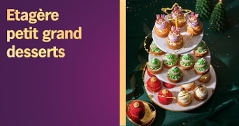 Etagère met feestelijke kleine desserts in kerstthema op een marmeren standaard, met decoratieve bomen en gouden accenten op de achtergrond