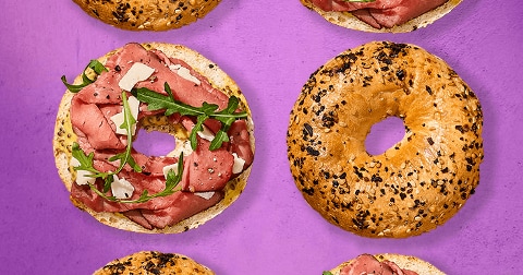 Bagels, waarvan sommige geopend en belegd met rosbief, rucola en Parmezaanse kaas, op een paarse achtergrond.