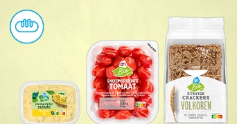 Drie Albert Heijn producten: plantaardige salade, bakje biologische snoepgroente tomaat en zak biologische volkoren crackers met sesam, lijnzaad en zonnebloempitten op een lichtgele achtergrond.