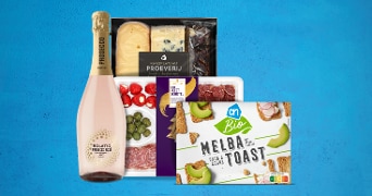 Flessen Solatio prosecco rosé, kaasplateau, feestschotel met worst en gevulde pepers, en AH Bio melba toast op een blauwe achtergrond