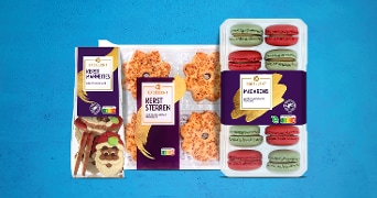 Albert Heijn Excellent kerstmannetjes, kerststerren en macarons verpakkingen op een blauwe achtergrond