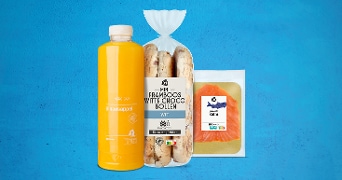 Fles verse sinaasappelsap, zak mini framboos witte choco bollen en verpakking gerookte zalm van Albert Heijn op een blauwe achtergrond