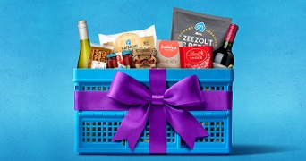 Blauwe Albert Heijn krat gevuld met diverse producten zoals wijn, chocolade, crackers en zoutjes, versierd met een paarse strik op een blauwe achtergrond