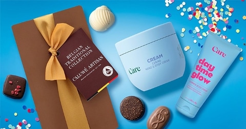 Een geschenkdoos met Belgische pralines van Caluwé Artisan, omringd door Care hand- en bodycrème, Care bodycrème 'day time glow', diverse pralines en kleurige confetti op een blauwe achtergrond.