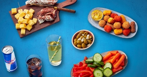 Borrelplank met kaasblokjes, droge worst, olijven, diverse snacks en drankjes, waaronder Red Bull.