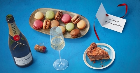 Feestelijke opstelling met Moët & Chandon champagne, kleurrijke macarons en een stuk taart, gepaard met een felicitatiekaart.