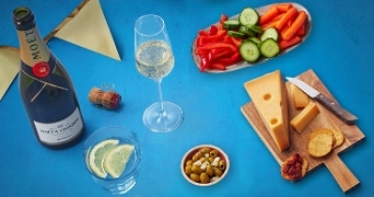 Fles Moët & Chandon champagne met hapjes zoals kaas, gesneden paprika, komkommer, wortel, olijven en citroenschijfjes op een blauwe achtergrond.