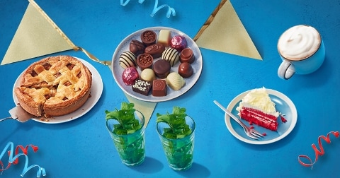 Taart, bonbons, een stuk red velvet cake, twee munttheeën en een cappuccino op een feestelijke tafel.