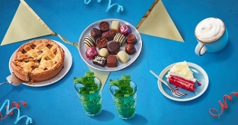 Taart, bonbons, een stuk red velvet cake, twee munttheeën en een cappuccino op een feestelijke tafel.