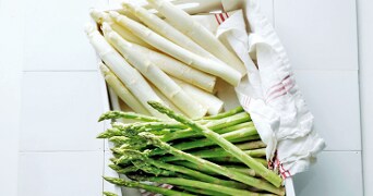 Groene en witte asperges op een witte schaal met een theedoek.