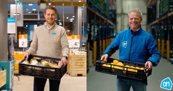 Twee Albert Heijn medewerkers dragen kratten met groenten en fruit in een winkel en een magazijn.
