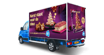 Albert Heijn bestelwagen met kerstadvertentie "Kerst staat voor de deur", toont feestelijke desserts en allerhande magazine-cover.