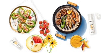 Zomerse barbecue setting met salade, aardbeien, gesneden meloen, gegrilde groenten, vlees op de grill en Care zonbeschermingsproducten.