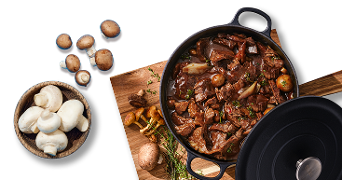 Stoofpot met rundvlees, champignons en kruiden, geserveerd in een zwarte pan op een houten plank, met verse champignons ernaast