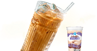 IJskoffie macchiato van Albert Heijn in glas met ijsblokjes en een rietje, naast een beker verpakking