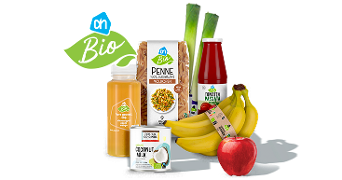 Assortiment van biologische Albert Heijn producten, waaronder volkoren penne, tomatenpassata, vers geperste sinaasappelsap, kokosmelk, bananen, prei en een rode appel.