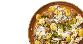 Gnocchi met courgette, bloemkool, rode ui, gehaktballetjes en geraspte kaas op een bruin bord