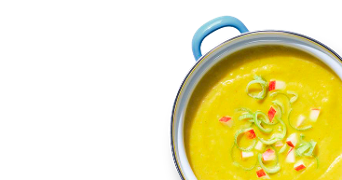 Gele groentesoep in een pan, gegarneerd met stukjes appel en prei