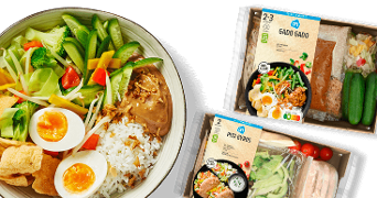 Grote schaal met gado gado gerecht met rijst, groenten, ei en pindasaus, naast Albert Heijn maaltijdpakketten voor gado gado en pita gyros.