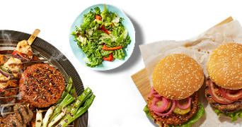 Gegrilde groenten, hamburger en spies op een barbecue, een bord salade en twee hamburgers met sla en tomaat op een houten plank.
