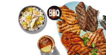 BBQ gevogelte- en vleesgerechten op een blauw bord, samen met een bowl huzarensalade met druiven en ei, en een glas koude drank met ijs en limoen.