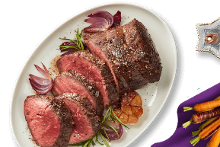 Rosbief op een schaal met rode ui en knoflook, daarnaast een bos kleurrijke wortels op een paarse doek en een stervormige kaars.