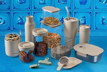 Verschillende beige bewaardozen, flessen en potten met etenswaren zoals koekjes, muesli en zaden op een blauw oppervlak, met Delfts blauwe tegels op de achtergrond.