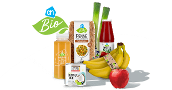 Albert Heijn Bio producten, waaronder volkoren penne, kokosmelk, tomatenpassata, een fles vers geperst sap, prei, bananen en een rode appel, bij elkaar gepresenteerd