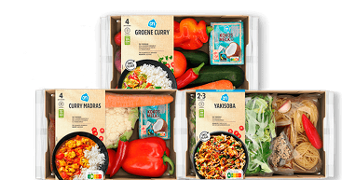 Drie maaltijdpakketten van Albert Heijn, waaronder Groene Curry, Curry Madras en Yakisoba, met verse groenten en ingrediënten in kartonnen dozen.