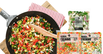 Roerbakgroenten in een pan met een houten lepel, naast verpakkingen AH roerbakmix Italiaans en Chinees.