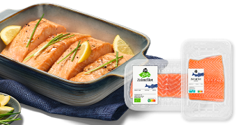 Gebakken zalmfilets in een ovenschaal met citroenpartjes en verse kruiden, naast twee verpakkingen AH Zalmmfilet, waaronder biologische variant.