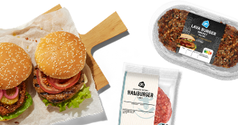 Twee versgebakken hamburgers met sla, ui en tomaat op een houten plank, naast verpakkingen van Albert Heijn hamburger en AH Lava Burger Smokey.