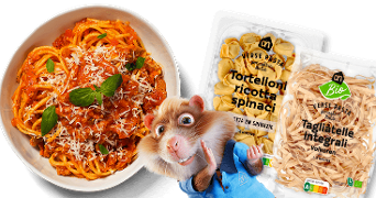 Pastagerecht met tomatensaus en basilicum in een kom, naast verpakkingen van AH Verse Pasta Tortelloni ricotta spinaci en AH Biologische Tagliatelle volkoren, met het Albert Heijn hamstermascotte op de voorgrond.