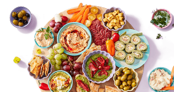 Borrelplank met verschillende smeersels, groenten, kaasblokjes, druiven, olijven, wraps, toastjes en charcuterie