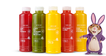 Vijf flessen AH vers sap in verschillende smaken en kleuren, met daarnaast een kind verkleed als paashaas.