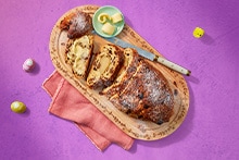 Gesneden stolbrood met rozijnen en amandelspijs op een houten plank, met een schaaltje boter en een mes.