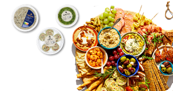 Borrelplank met diverse hapjes, waaronder blauwe druiven, groene druiven, olijven, diverse soorten vleeswaren, wraps, spreads en toastjes. Links zijn verpakkingen van Albert Heijn Excellent knoflooksaus, groene pesto en wraps met kipfilet en roomkaas te zien.