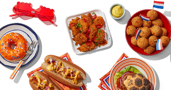 Assortiment van Nederlandse snacks en gerechten, waaronder bitterballen met vlaggetjes, een hamburger, hotdogs met saus, pittige kipstukjes, een donut met oranje glazuur en strooidecoratie, gele saus in een bakje en rode lolly's in de vorm van handen.